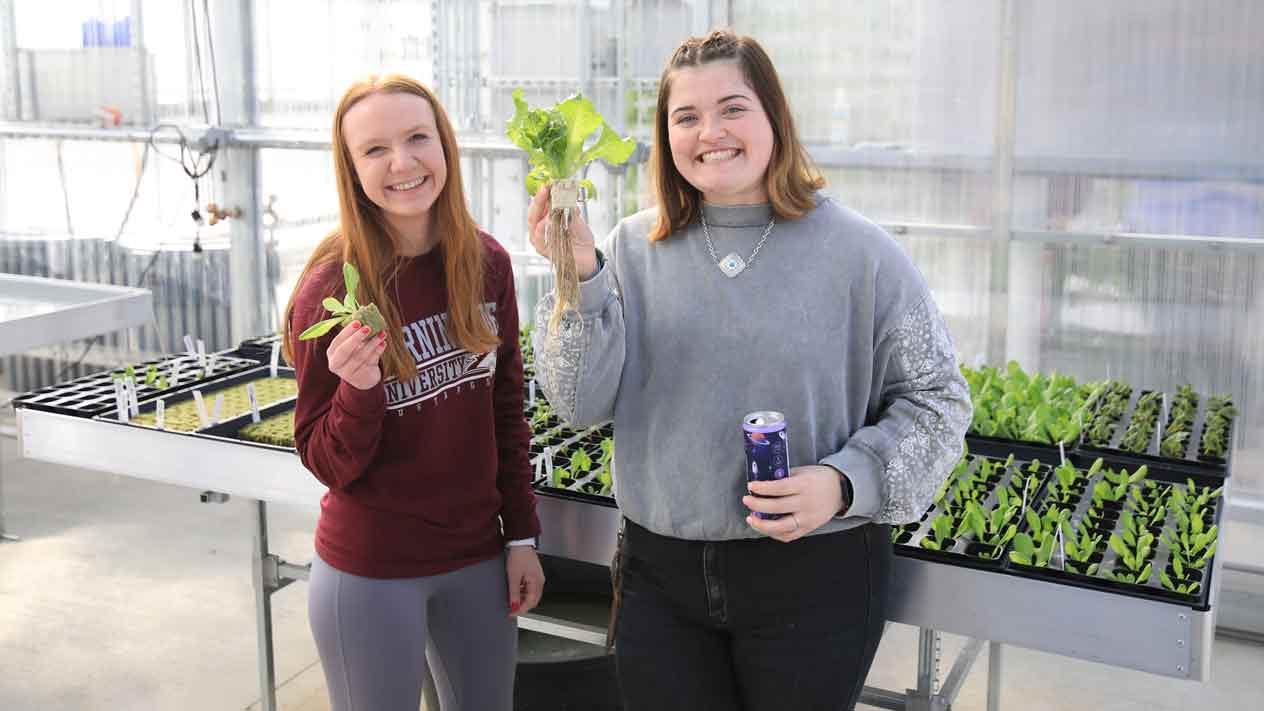 Two students in the greenhouse holding plants